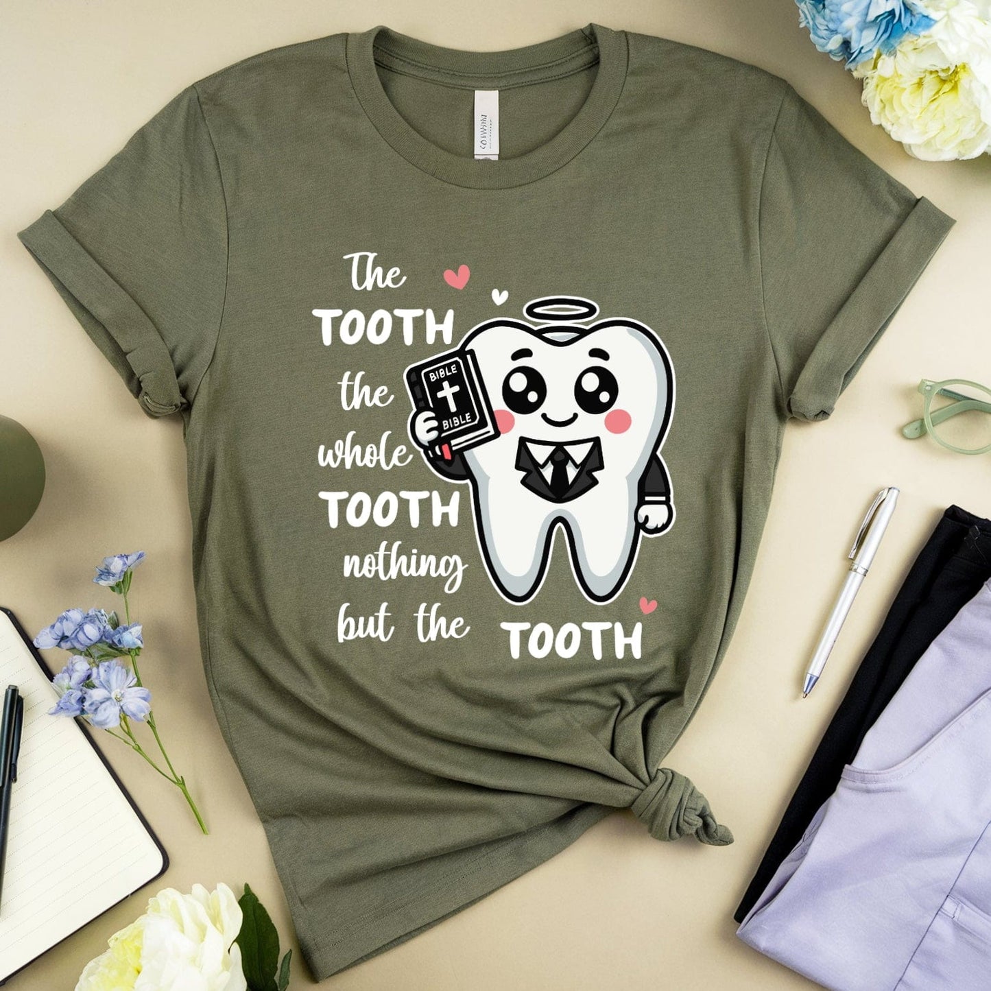 Green t-shirt with a tooth graphic and text on a table with flowers and a mug.