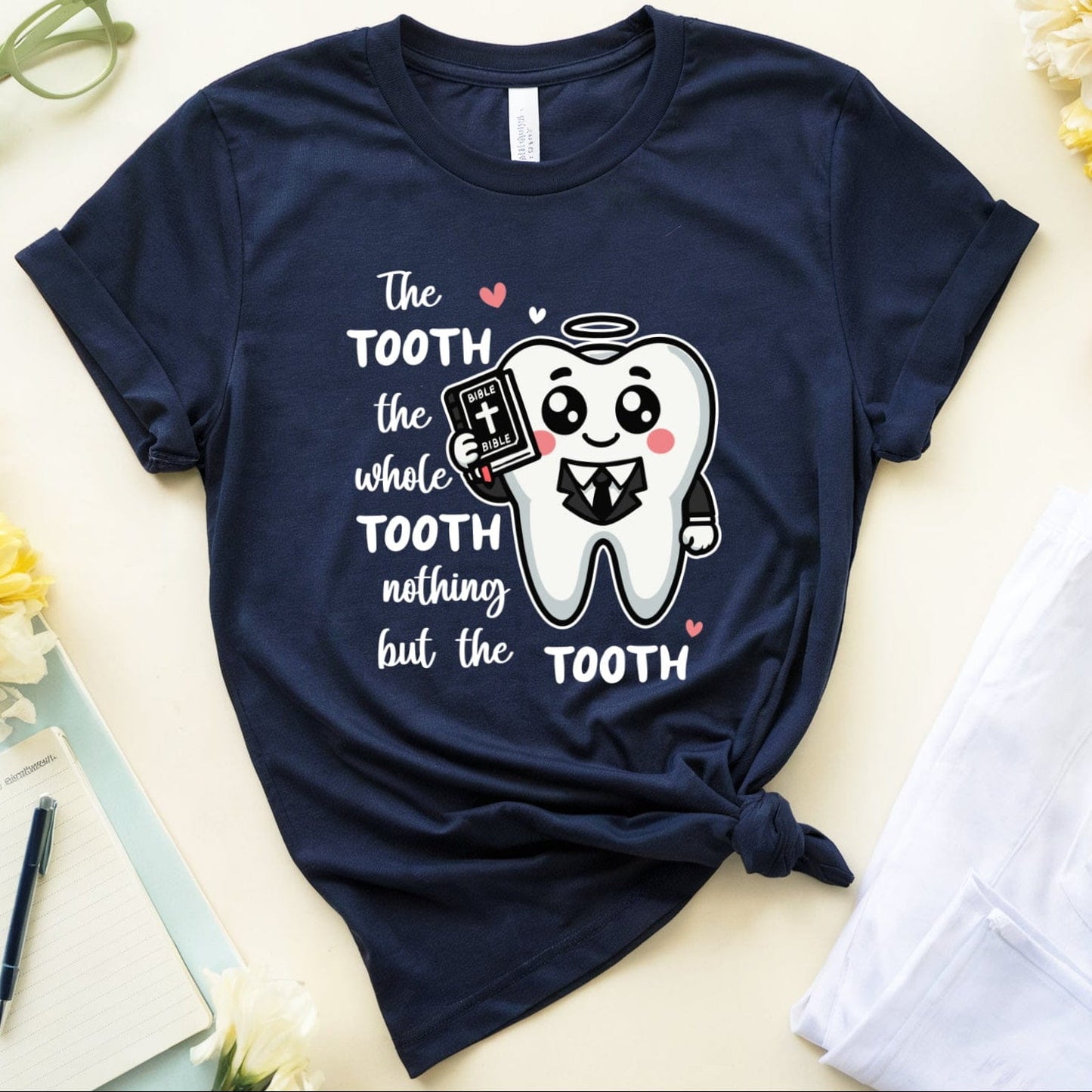 Navy blue t-shirt with a tooth graphic and text on a light surface with flowers and glasses.