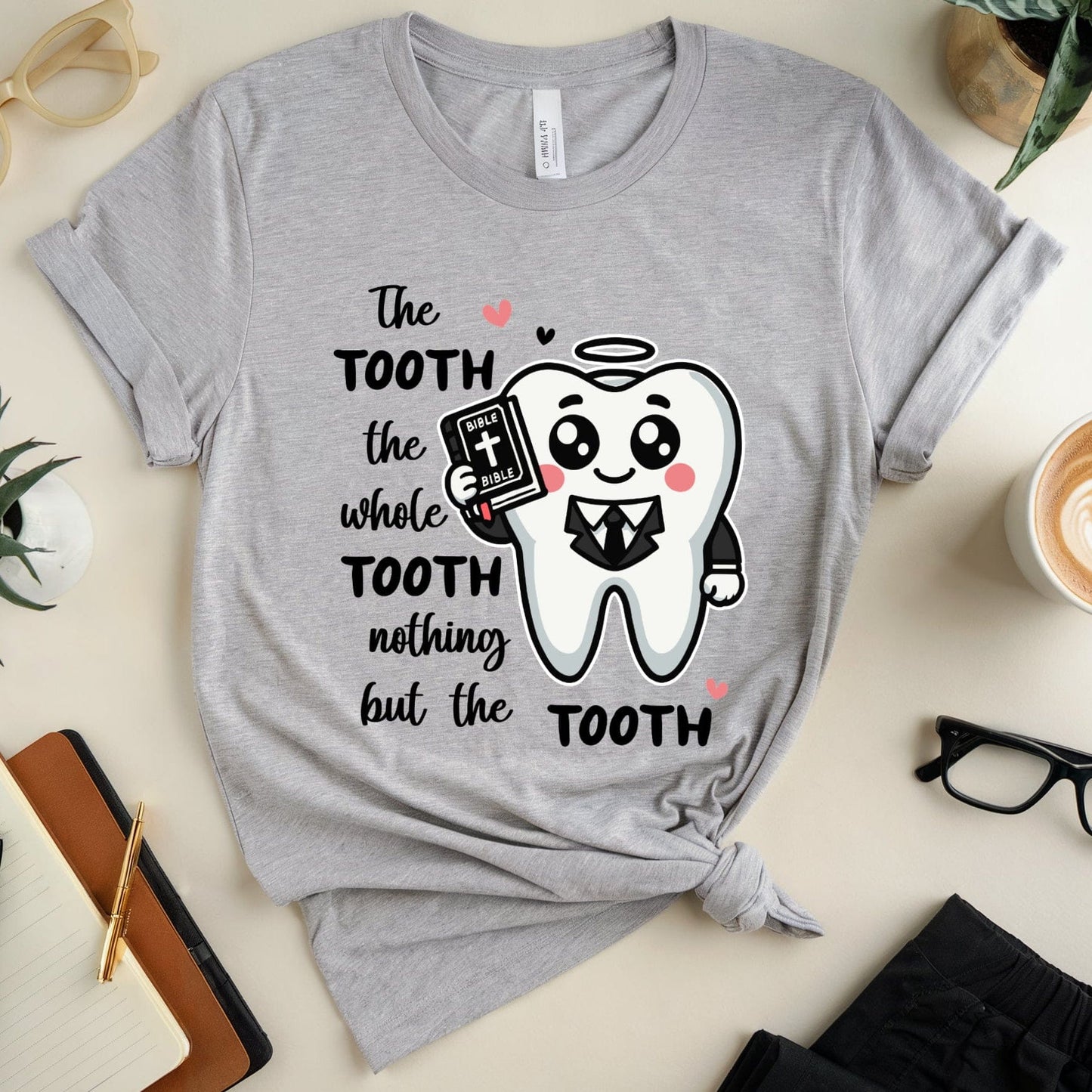Gray t-shirt with a cartoon tooth graphic and text on a table with accessories.
