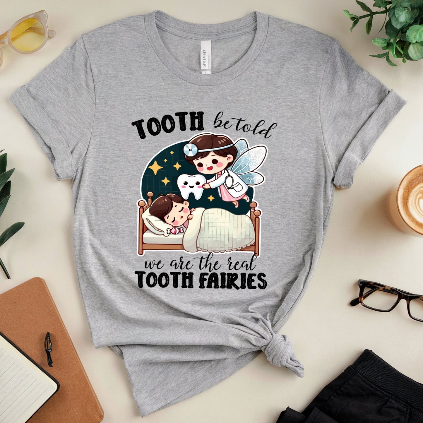 Gray t-shirt with a cartoon design of children and tooth fairies on a light surface with accessories.