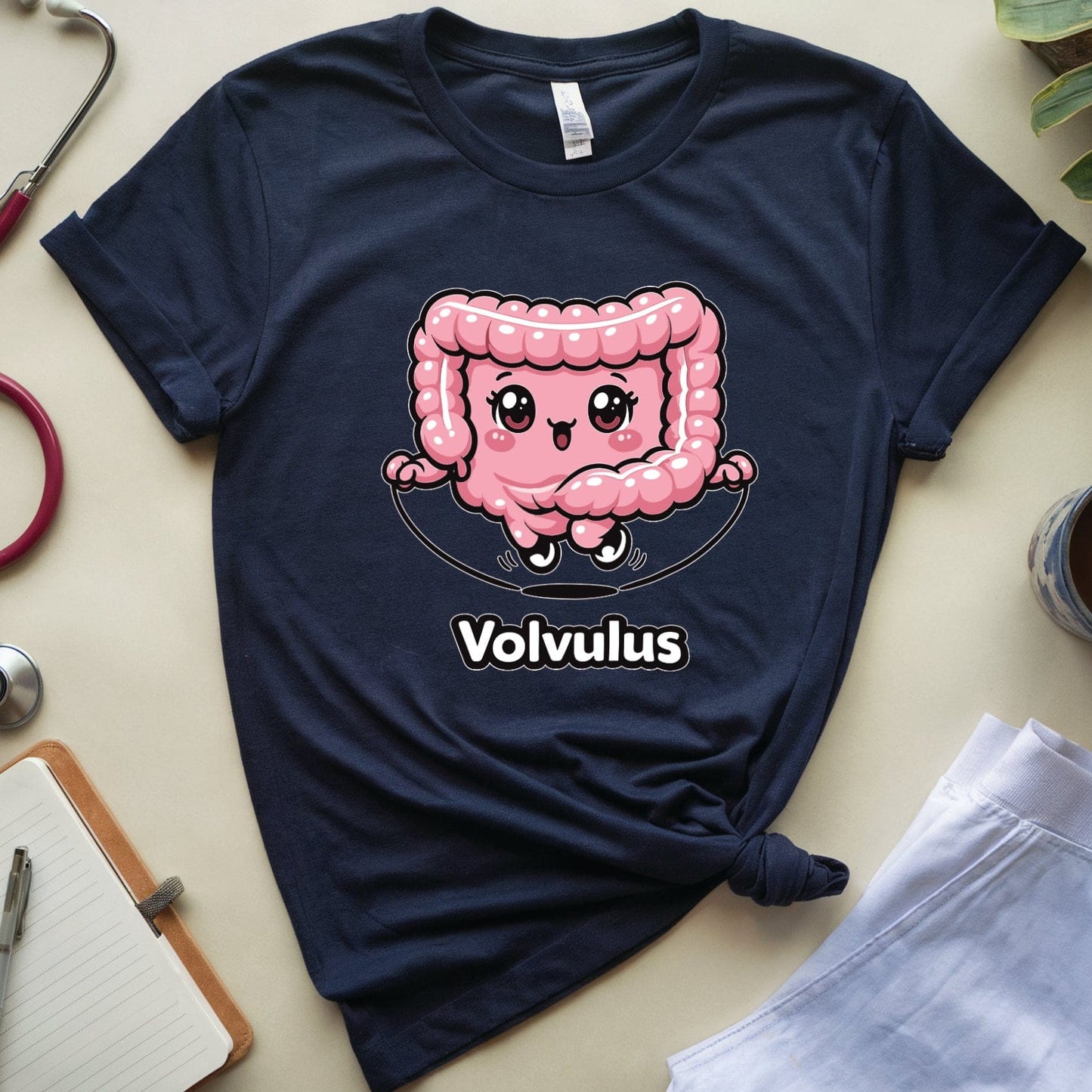 Navy blue t-shirt with a pink cartoon character and 'Volvulus' text on a light surface with medical-themed items.
