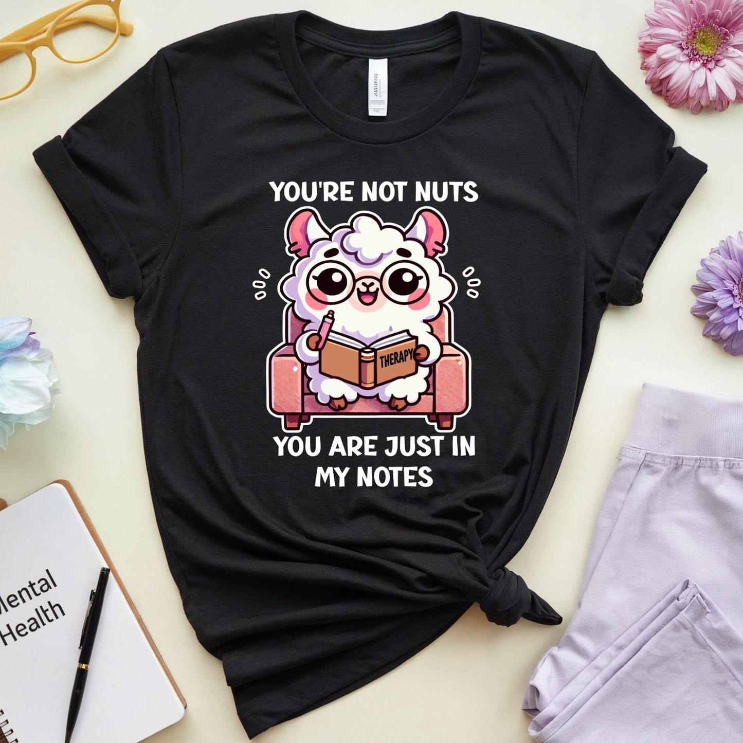 Black t-shirt with cartoon design and text on a light surface with flowers and glasses.