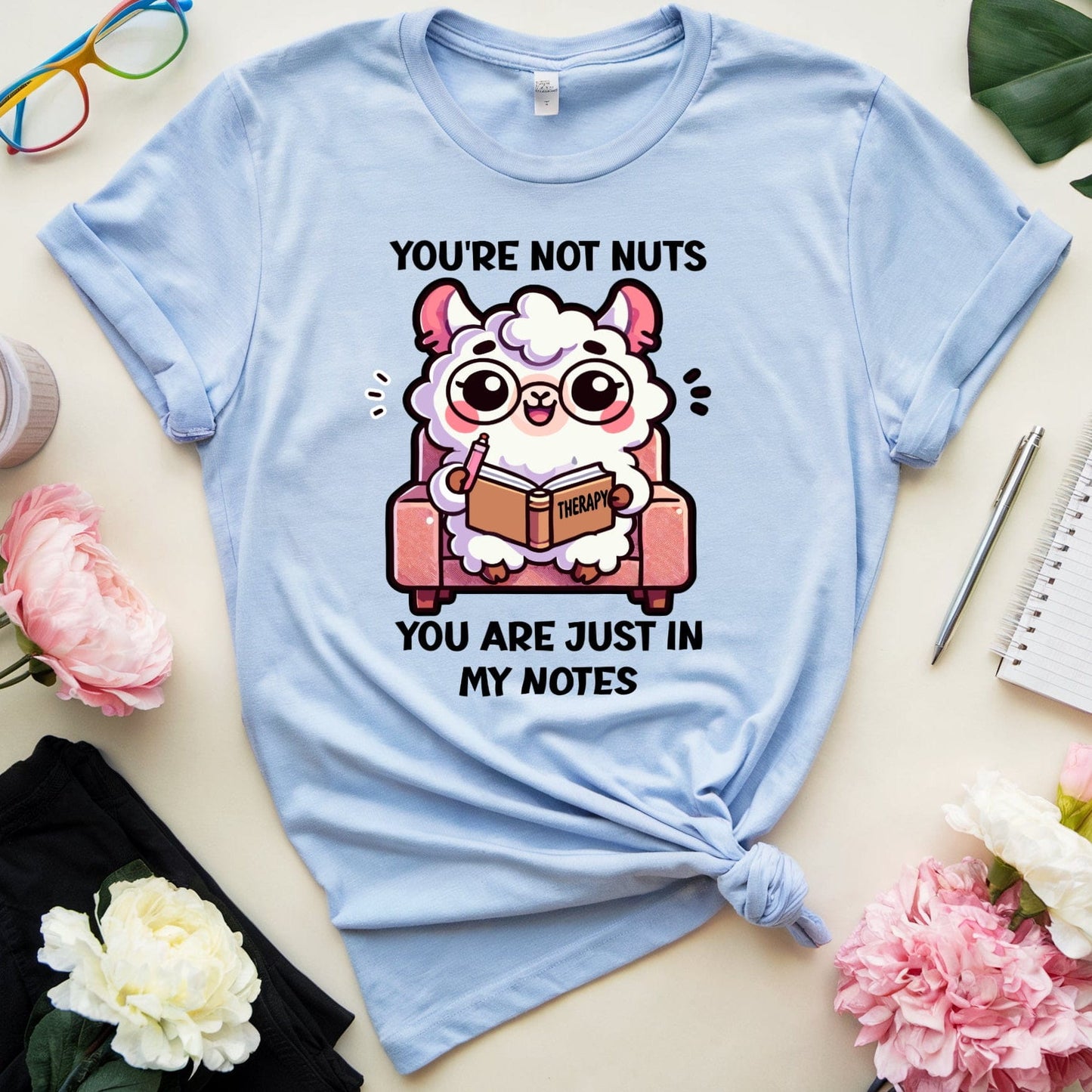 Light blue t-shirt with cartoon character and text on a table with flowers and glasses.