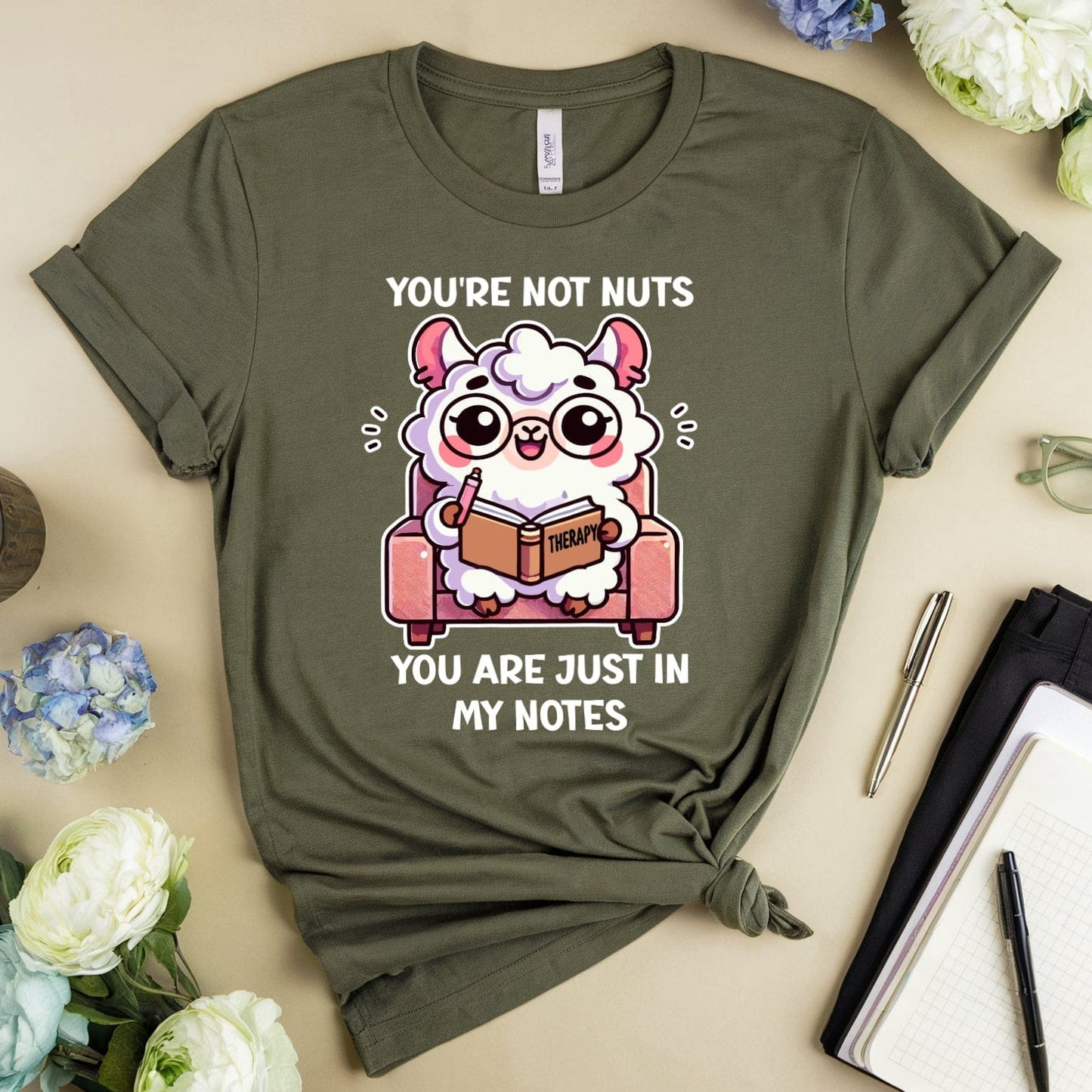 Green t-shirt with cartoon character and text on a beige surface with flowers and a mug.