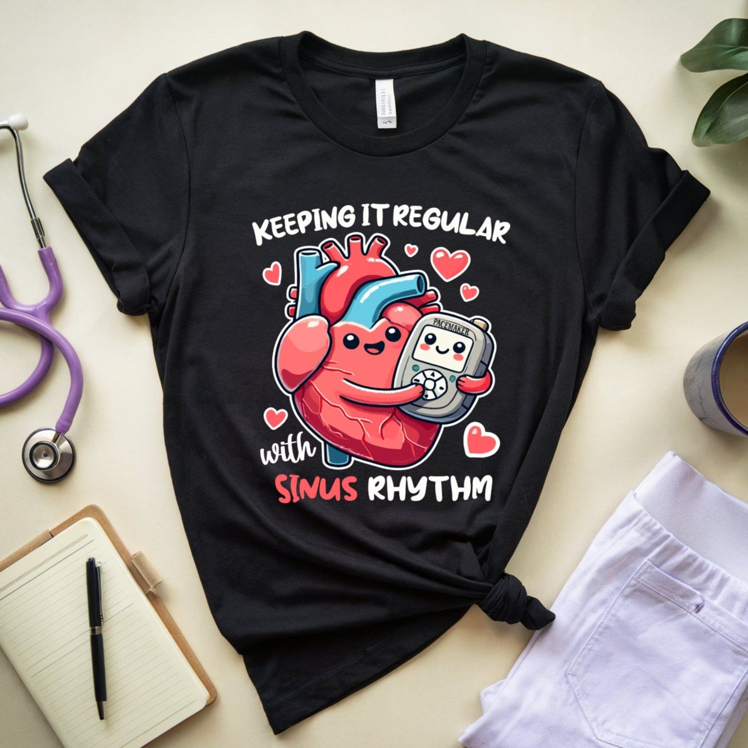 Black t-shirt with a heart graphic and text for cardiology on a light surface with medical-themed items.