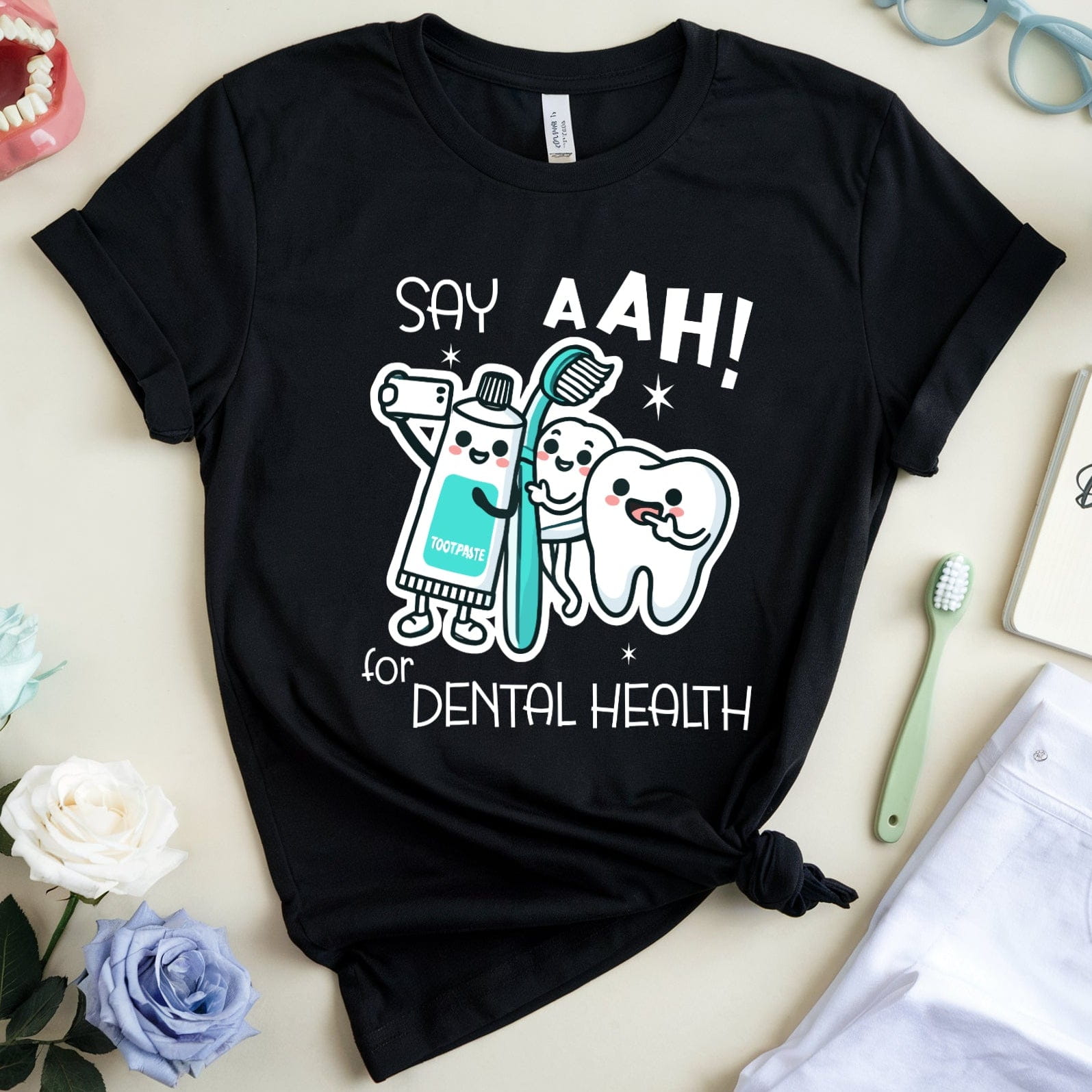 Black t-shirt with dental-themed design on a light surface with flowers and dental tools.