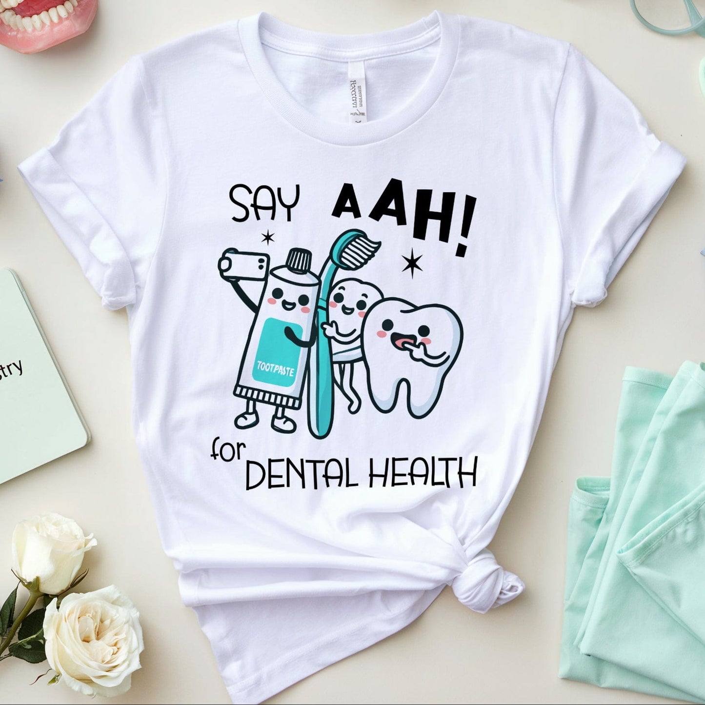 White t-shirt with dental-themed design on a table with dental-themed items.